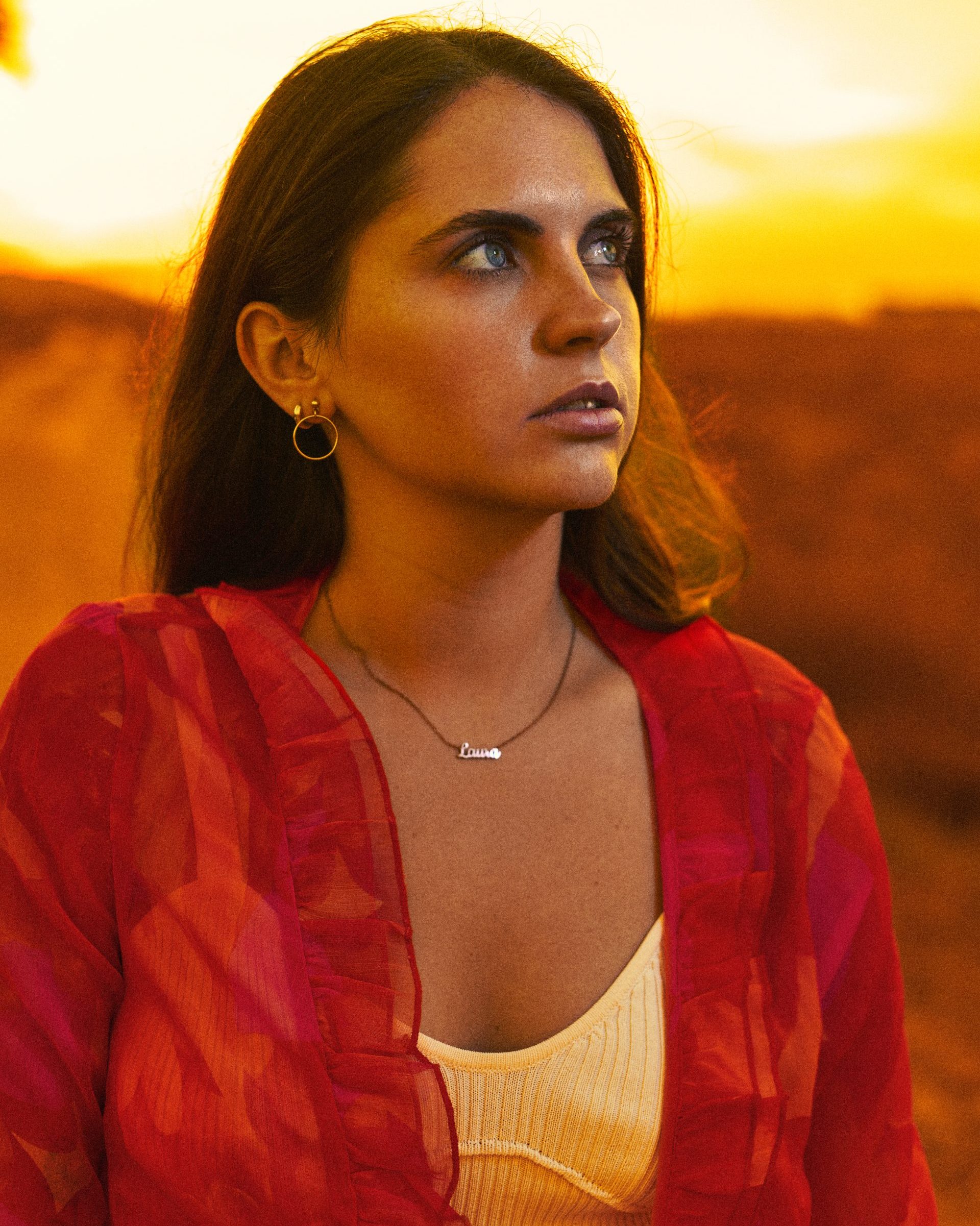 Retrato de una mujer con ojos azules y blusa roja, retocado con técnicas de color grading para crear un fondo de atardecer cálido y potenciar el contraste cromático.